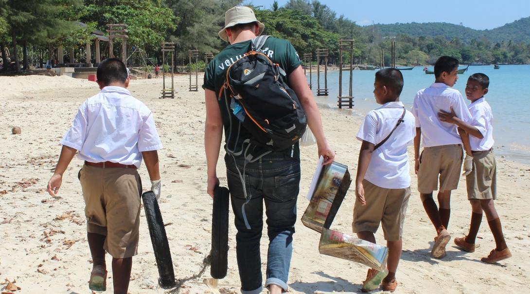 A Projects Abroad volunteer works with school children on a beach clean-up during his conservation volunteering in Thailand for high school students A high school student volunteer picks up litter on the beach to promote marine conservation in Thailand
